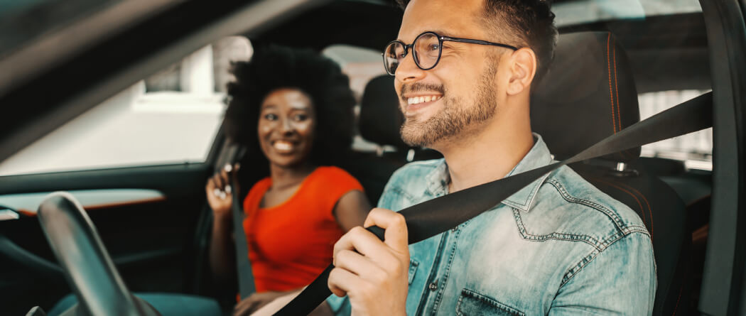 Two young adults buckling seat belts in a car